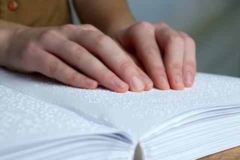 Das Foto zeigt die Hände einer Frau. Sie ließt ein Buch, welches in Brailleschrift geschrieben ist.