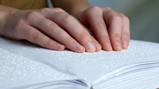 Das Foto zeigt die Hände einer Frau. Sie ließt ein Buch, welches in Brailleschrift geschrieben ist.