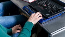 Eine Person nutzt einen Laptop mit Braillezeile und liest diese mit der rechten Hand.