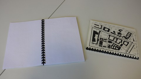 Photograph of the open book in ring binding with explanations of maps of individual city areas in Braille, plus tactile maps in a separate booklet