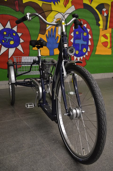 The photo shows one of the service tricycles, which is equipped with lights, a bell and a small luggage basket between the two rear wheels. The tricycle can stand upright without any problems.