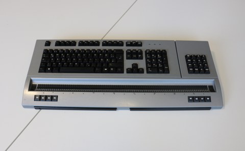 The photo shows the Mobile Braille Display 80s lying on the table, which consists of a combined standard and Braille keyboard.