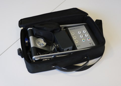 Photo shows the mobile whiteboard reader in the open case lying on the table. The camera can be aimed at documents or a blackboard, and there are various buttons for making settings. 