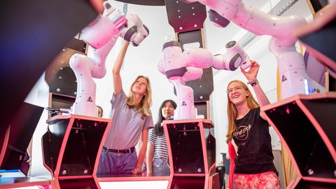 Drei junge Frauen bedienen Roboterarme.