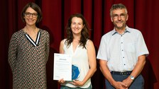 Three people are standing together and one person is holding an award.