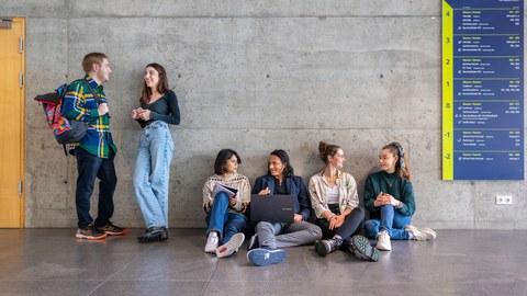 Fotos von 4 auf dem Boden sitzenden und 2 stehenden sich unterhaltende Studierenden in einem TUD-Gebäude