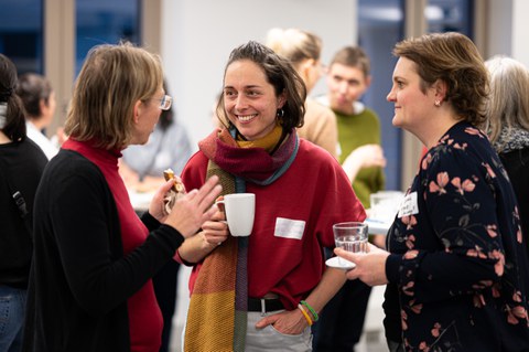 Three women chat and laugh at the New Year's reception of the Women@DDc network. They hold cups and glasses in their hands.