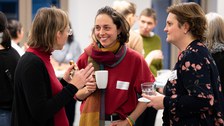 Three women chat and laugh at the New Year's reception of the Women@DDc network. They hold cups and glasses in their hands.