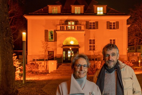 Rektorin Staudinger und Prorektor Kobel stehen vor dem orange erleuchteten Rektorat. Es beteiligt sich damit am Orange the Day um auf Gewalt gegen Frauen aufmerksam zu machen.