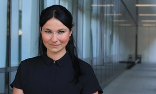 A dark-haired person can be seen in the portrait view. She is standing in a corridor in front of a window.