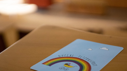 A postcard for the "Queer Parenthood" event series is on a table in the lecture hall. 