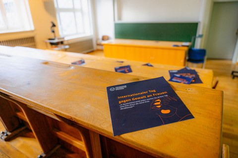 Ein Foto in einen Hörsaal, auf einer Bank liegt ein Flyer mit der Aufschrift Internationaler Tag gegen Gewalt an Frauen