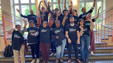 A group of people wearing all the same shirt and looking happy. They are throwing their hands in the air.