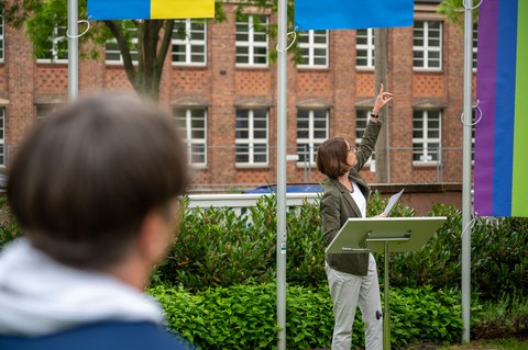 Prorektorin Böhm steht am Redner:innenpult und zeigt auf Flagge.