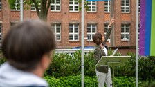 Prorektorin Böhm steht am Redner:innenpult und zeigt auf Flagge.