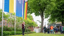 Fay Uhlmann steht neben 3 Flaggen und Publikum schaut Fay Uhlmann zu