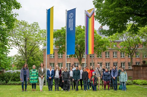 Eine Gruppe von Menschen stehen im Rektoratsgarten vor der Progressive Pride Flag, die TU Dresden Fahne, sowie die Ukrainefahne