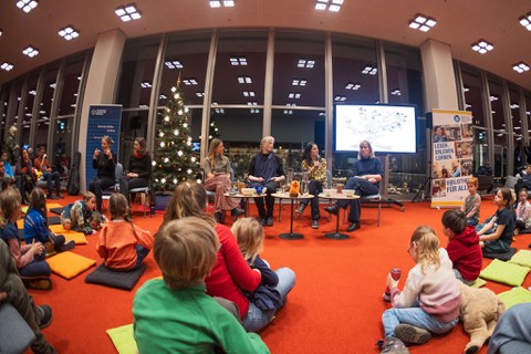Vier Frauen und die beiden Gebaärden Dolmetscherinnen sind auf dem Podium zu sehen. Vor Ihnen auf dem Boden sitzen einige Kinder.
