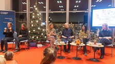 Sechs Frauen sitzen vor einer weihnachtlichen Kulisse auf dem Podium. Die beiden Frauen links gebärdendolmetschen.