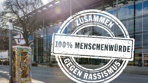 Das Foto zeigt das Hörsaalzentrum von außen (Vorderansicht). Auf das Foto wurde eine Grafik gesetzt. Es ist das Logo der Internationalen Wochen gegen Rassismus.