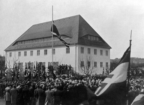 Historische schwarz-weiß Fotoaufnahme, die das Fahnenhissen zur Einweihung des Hauses des NS-Studentenbundes im April 1936 zeigt.