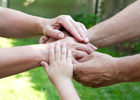 Auf dem Foto sieht man die Hände mehrerer Personen unterschiedlichen Alters, die übereinander liegen und sich gegenseitig halten.