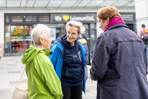 3 Personen stehen zusammen und unterhalten sich. Eine der Personen trägt einen dunkelblauen Hoodie mit der Aufschrift Technische Universität Dresden.