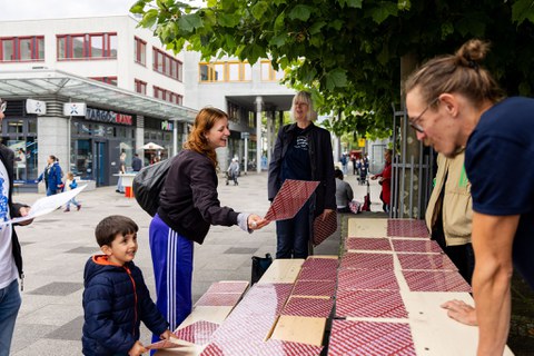 Das Foto zeigt einen kleinen Jungen und Erwachsene, die an Festzelttischen und -bänken stehen. Auf den Bänken und Tischen liegen Karten. Der Junge und eine der Erwachsenen halten jeweils eine Karte in der Hand. 