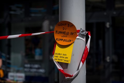 An einem Pfosten steht auf einer farbigen Karte "Womit bist du Klimaheld:in? Womit Klimakiller?