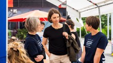 Drei Personen stehen unter einem Pavillon und unterhalten sich. 