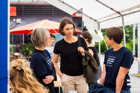 Drei Personen stehen unter einem Pavillon und unterhalten sich. 