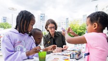 Drei Kinder und eine erwachsene Person sitzen an einem Tisch und basteln. 