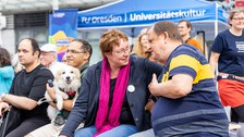 Menschen sitzen auf Bänken und unterhalten sich. 