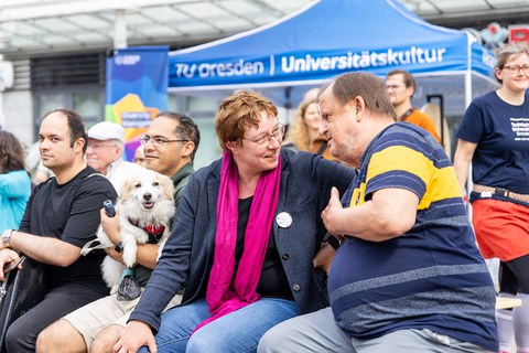Menschen sitzen auf Bänken und unterhalten sich. 