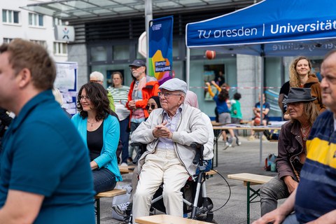 Menschen unterschiedlichen Alters sitzen auf Bänken, die hintereinander stehen. 