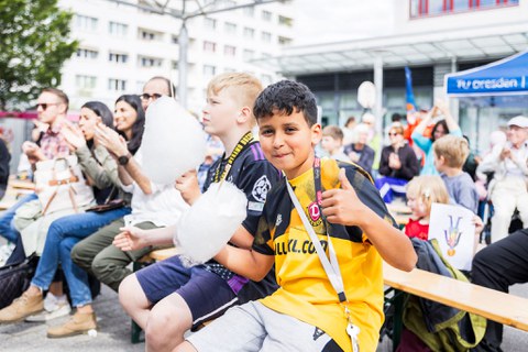 Personen sitzen auf Festzeltbänken. Zwei Jungs im Vordergrund essen Zuckerwatte. 