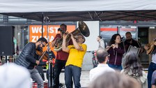 Musiker:innen mit verschiedenen Instrumenten spielen zusammen unter einem Pavillon.