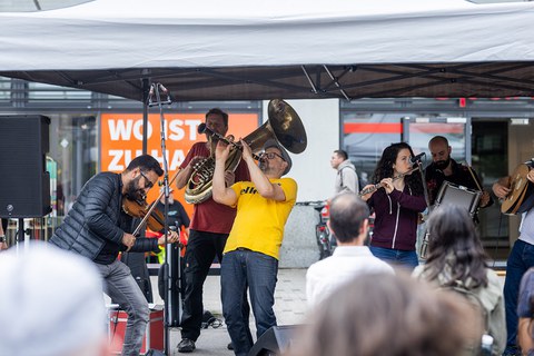 Musiker:innen mit verschiedenen Instrumenten spielen zusammen unter einem Pavillon.