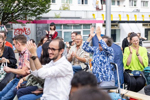 Menschen sitzen auf Festzeltbänken, lächeln und klatschen. 
