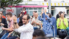 Menschen sitzen auf Festzeltbänken, lächeln und klatschen. 