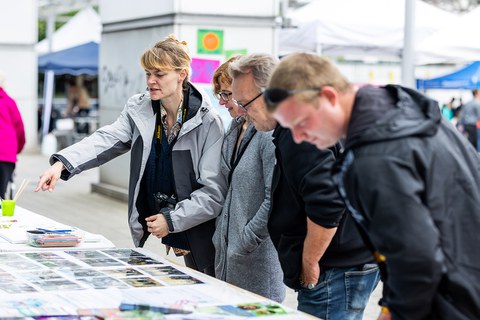 4 Personen stehen an einem Festzelttisch, auf dem Fotos liegen. 