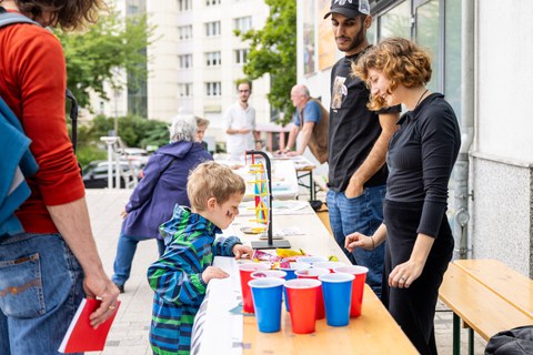 1 Kind und Erwachsene stehen an einem Festzelttisch, auf dem rote und blaue Becher stehen. 