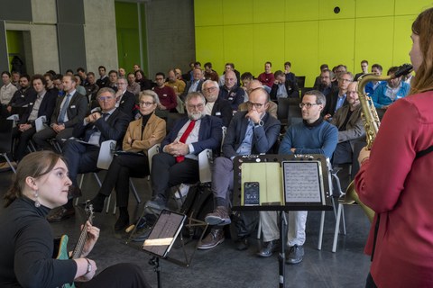 Publikum während einer musikalischen Einlage; im Vordergrund zwei Musikerinnen 