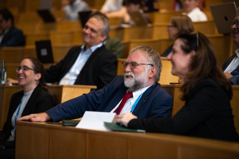Foto von v.l.n.r.: Prof. Diana Göhringer (TUD), Prof. Martin Schulz (TUM), Prof. Wolfgang E. Nagel (TUD) und Prof. Heike Graßmann (Sächsische Staatssekretärin im SMWKT) als Zuhörende lachend im Auditorium. Im Hintergrund - verschwommen - weitere Zuhörende