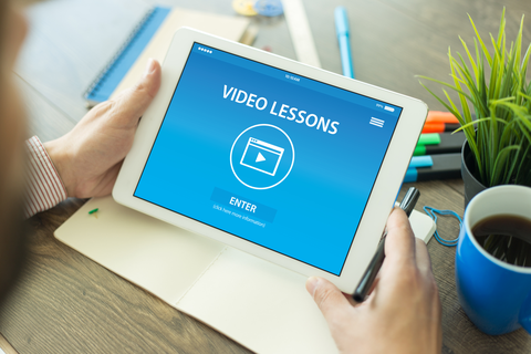 oto: Mann am Arbeitsplatz, der auf ein Tablet blickt auf dem steht "Video Lessons", ein Play-Pfeil und "ENTER".