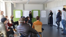 Poster Session, Austausch mit der Praxis, 5 Personen stehen vorne neben den Postern und präsentieren vor Publikum