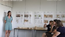 Poster Session, Austausch mit der Praxis, an der Wand hängen Poster, eine Frau steht vorne, 3 Frauen sitzen gegenüber