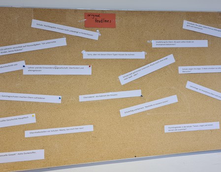 Das Foto zeigt eine Pinnwand weißen rechteckigen beschriebenen Zetteln, die daran gepinnt wurden. In der Mitte der oberen Kante befindet sich ein roter  Zettel, mit dem Text: „original Headlines“. 
