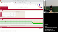 Screenshot einer Online-Vorlesung. Im linken Teil des Bildes ist eine Website namens „AnimOS CPU-Scheduling“ zu sehen. Auf der rechten Seite sieht man das Videostandbildes einer Person vor einer Tafel, vor der Person steht ein Bildschirm.