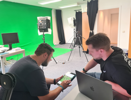 Zwei Menschen arbeitend vor Computern, in einem Raum mit Greenscreen 